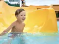 Ein Junge mit blauen Augen lacht fröhlich im Wasser der Wasserrutsche im Heidebad Torgelow.