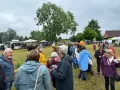 Menschen genießen das inselfest Mirow bei bewölktem Himmel. Stände und Bäume säumen die grüne Wiese.