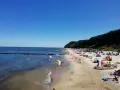 Sonniger Tag am Strand Koserow mit vielen Badegästen, bunten Sonnenschirmen und spielenden Kindern im flachen Wasser.