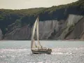 Segelboot gleitet über glitzerndes Wasser vor Kreidefelsen und grünen Wäldern. Ein Tag zum Ostsee segeln.