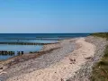 Ein ruhiger Tag am Dranske Strand. Holzpfähle ragen aus dem ruhigen Meer, das sich unter einem klaren blauen Himmel erstreckt.