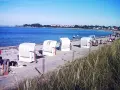 Strandkörbe am Ostseestrand, im Hintergrund der glowe hafen mit Häusern und Bäumen.