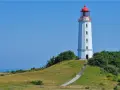Der Leuchtturm Dornbusch ragt auf einer grünen Anhöhe empor, mit dem blauen Meer im Hintergrund. Eine Treppe führt zum Eingang.