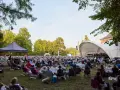 Großes Publikum bei einem Open-Air-Konzert im Rahmen eines **Festivals Mecklenburg-Vorpommern**. Eine Bühne mit Orchester, viele Sitzende auf Rasenflächen.