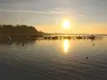 Sonnenaufgang am **Stralsund Strand**. Boote liegen am Steg, die Sonne spiegelt sich im ruhigen Wasser.