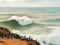 Riesige Welle bricht vor Zuschauern am mole strand. Ein Surfer reitet die Welle.