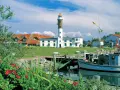 Idyllischer Hafen mit Leuchtturm auf Insel Poel, ein echter Geheimtipp. Boote liegen im Wasser, rote Rosen blühen.
