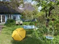 Ein Garten mit blauem Haus, gelbem Regenschirm (Kunst Offen) und Glaskunst auf einem Tisch. Pfingsten 2026 MV.