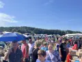Buntes Treiben auf dem Flohmarkt Sellin. Menschen stöbern an Ständen unter blauem Himmel, im Hintergrund ein Wald.