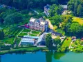 Luftaufnahme des schaugarten am tiefwarensee mit Gewächshäusern, einem Hauptgebäude und gepflegten Gärten am Ufer.