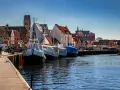 Boote liegen im **Wismar Hafen** vor bunten Häusern. Ein Schild wirbt für "Backfisch".