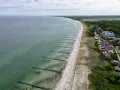 Luftaufnahme des Ahrenshoop Strandes mit Wellenbrechern, Sand und Bäumen. Ein Segelboot ist auf dem Meer zu sehen.