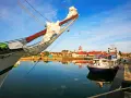 Ein Segelschiff im Vordergrund, im Hintergrund die Stadt Wolgast mit roten Dächern und einem Turm. Ein kleines Boot mit dem Namen "Wolgast" liegt am Kai.