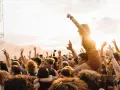 Menschen jubeln auf einem Festival in Rostock. Eine Frau sitzt auf den Schultern eines anderen Besuchers, während die Sonne untergeht.