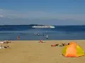 Sonne, Sand und ein Schiff auf dem Wasser – ein entspannter Tag am Schweriner Strand mit Badegästen und einer bunten Strandmuschel.