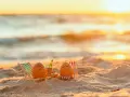 Zwei bemalte Eier entspannen sich in Liegestühlen am Strand bei Sonnenuntergang. Eine Flasche Sekt steht bereit. Eine süße Idee für Veranstaltungen an Ostern.