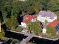 Luftaufnahme des Wasserschlosses Mellenthin mit Wassergraben, Brücke und umliegendem Park. Der Eintritt ist frei zugänglich.