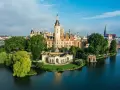 Schweriner Schloss auf einer Insel, umgeben von Wasser und grünen Bäumen. Ein Märchenschloss, das zu den Schwerin Geheimtipps zählt.