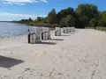 Reihe von Strandkörben am klink strand. Das Wasser glitzert im Hintergrund, Bäume säumen den Horizont.