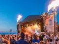 Feuerfontänen lodern bei Konzerten an der Ostsee. Eine Menschenmenge feiert am Strand zu elektronischer Musik.