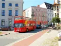 Roter Doppeldeckerbus für eine Stadtrundfahrt in Rostock fährt durch eine Gasse mit historischen Gebäuden.