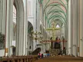 Imposanter Innenraum des Schweriner Doms mit Holzbänken, einem großen goldenen Kreuz und grünen Gewölben.