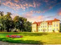 Gelbes Schloss mit roten Dächern, umgeben von grünen Bäumen und Blumenbeeten. Ein malerischer Anblick auf der Liebesinsel Mirow.