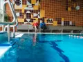 Zwei Männer sitzen in der Schwimmhalle Anklam auf einer Bank vor einer bunten Kachelwand mit Fischmotiven.
