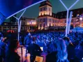 Konzert mit Sänger und Band auf der Bühne, beleuchtet von blauen Lichtern. Im Hintergrund die beleuchtete Architektur und eine Menschenmenge bei Veranstaltungen am Binz Kurplatz.