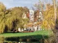 Herbstliche Farben umgeben das Wasserschloss Quilow. Ein Teich spiegelt die Bäume und das weiße Gebäude mit seinem markanten Turm.