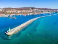 Leuchtturm am Ende einer Mole, die in das klare Wasser vor Sassnitz führt. Boote und die Stadt im Hintergrund.