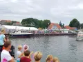 Menschen genießen das bunte Treiben beim Rock am Hafen. Boote liegen im Wasser, ein Rettungsboot fährt vorbei.