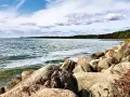 Felsen am kamminke strand mit Blick auf das ruhige Wasser und den grünen Wald am Horizont unter einem bewölkten Himmel.