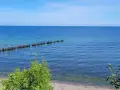 Ein ruhiger Tag am glühenden Strandpromenade. Das Meer ist ruhig, mit einer Reihe von Holzpfählen, auf denen Vögel sitzen.