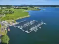 Der Hafen Sellin ist voller Segelboote, die auf dem ruhigen Wasser liegen. Im Hintergrund erstreckt sich eine grüne Landschaft mit Häusern und Bäumen.