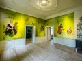 Ein Raum im Schloss Mirow mit Wandmalereien, die historische Persönlichkeiten und Karten zeigen. Ein Kachelofen steht rechts.