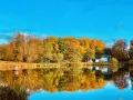 Herbstliche Farben im Schlosspark Putbus spiegeln sich im ruhigen Wasser. Ein kleiner Pavillon und ein modernes Gebäude säumen das Ufer.