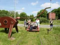 Eine Gruppe von Menschen auf einer Draisine Dargun, neben einer rostigen Skulptur.