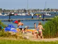 Familien genießen einen sonnigen Tag am Wasser. Kinder planschen, während Boote im Hintergrund ankern. Ein perfekter Ort für Seekamp Camping.