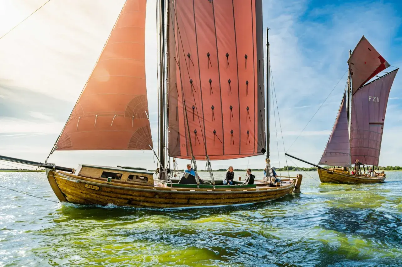 Zeesboot "Bill" segelt bei Ahrenshoop mit roten Segeln. Ein zweites Boot folgt.