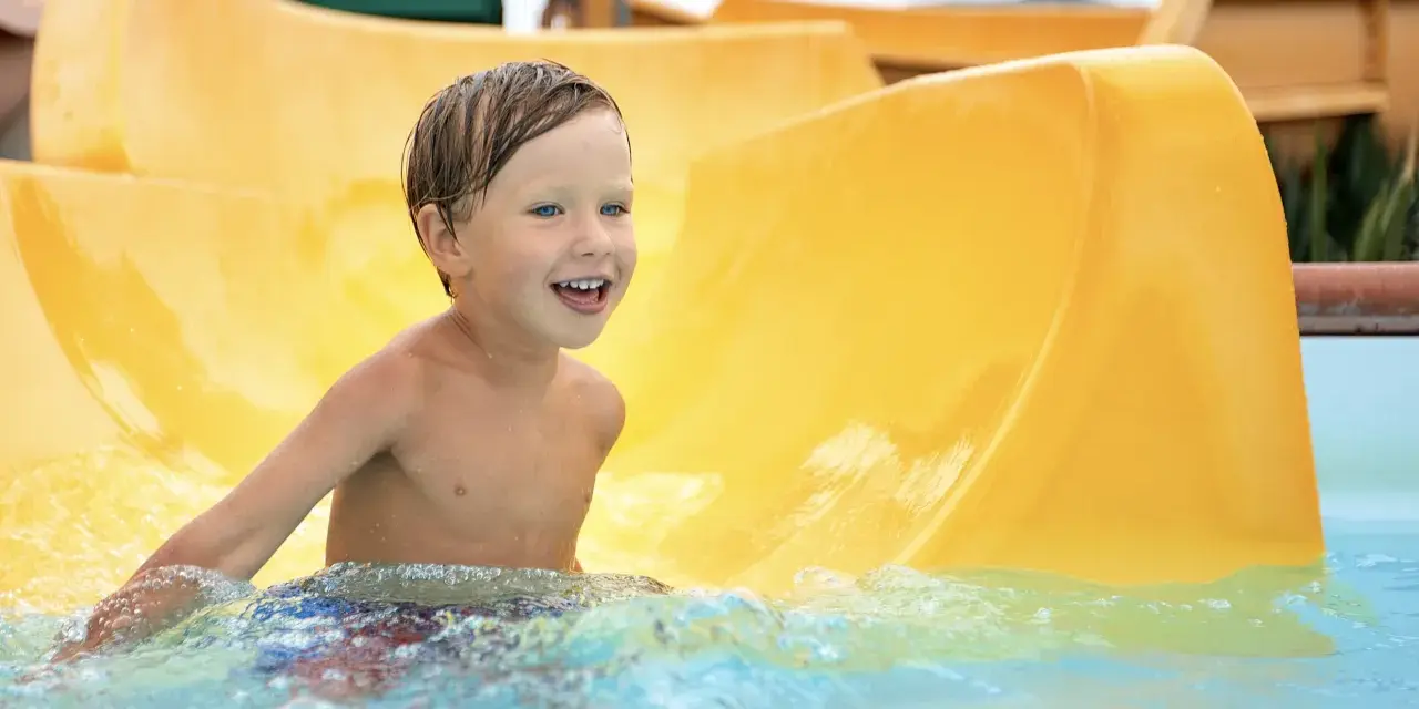 Ein Junge mit blauen Augen lacht fröhlich im Wasser der Wasserrutsche im Heidebad Torgelow.
