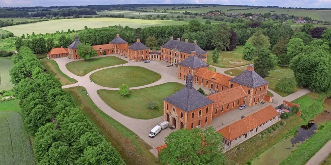 Luftaufnahme von Schloss Bothmer, einem barocken Anwesen mit roten Ziegelgebäuden, umgeben von grünen Gärten und Feldern.