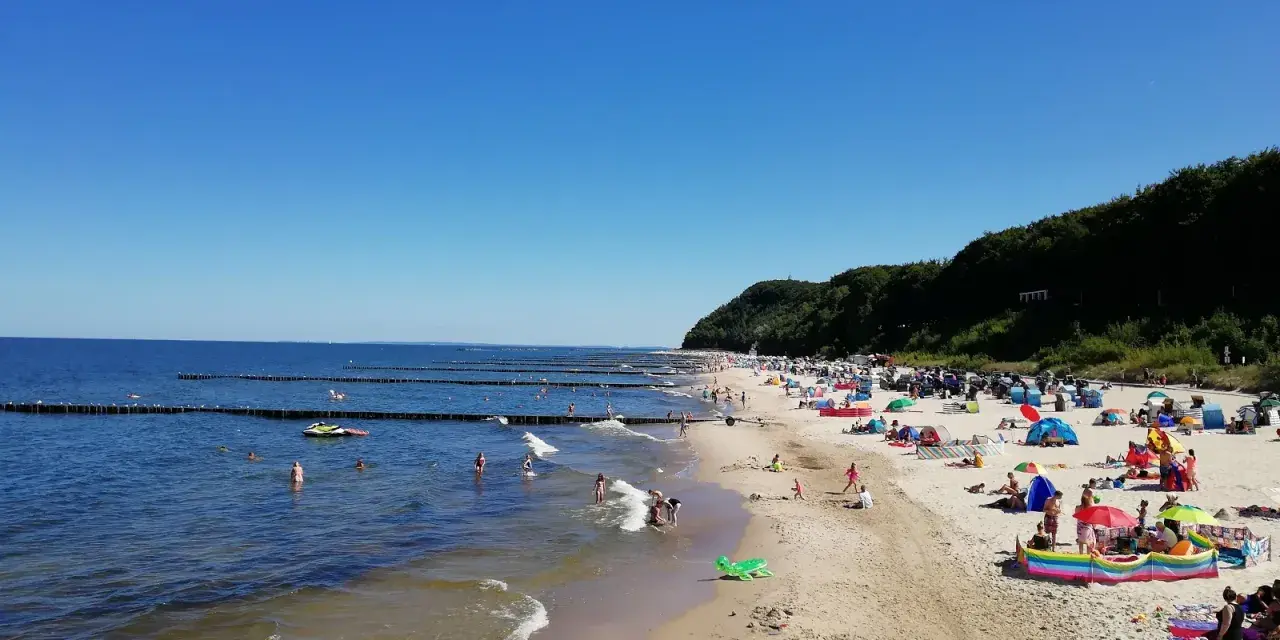 Sonniger Tag am Strand Koserow mit vielen Badegästen, bunten Sonnenschirmen und spielenden Kindern im flachen Wasser.