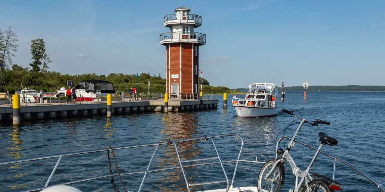 Plau am See: Leuchtturm und Promenade mit Booten. Ein Fahrrad wartet auf dem Vorderdeck.