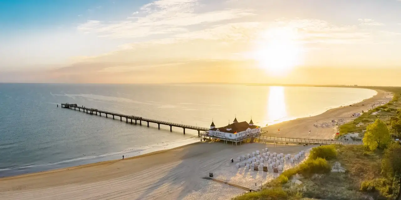 Sonnenuntergang am Ostsee Strand mit langer Seebrücke und Strandkörben.