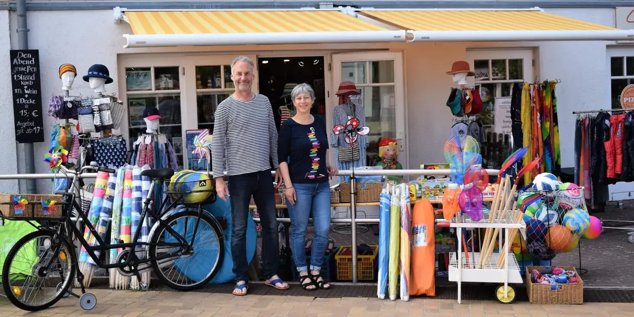 Ein Paar vor einem Laden mit Strandartikeln. Sie sind bereit, juliusruh einkaufen zu gehen und haben alles für einen schönen Tag am Meer.