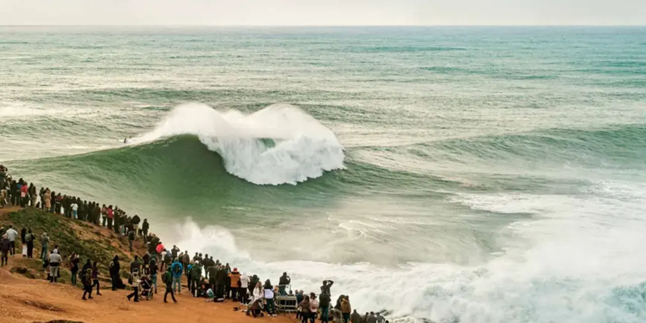 Riesige Welle bricht vor Zuschauern am mole strand. Ein Surfer reitet die Welle.