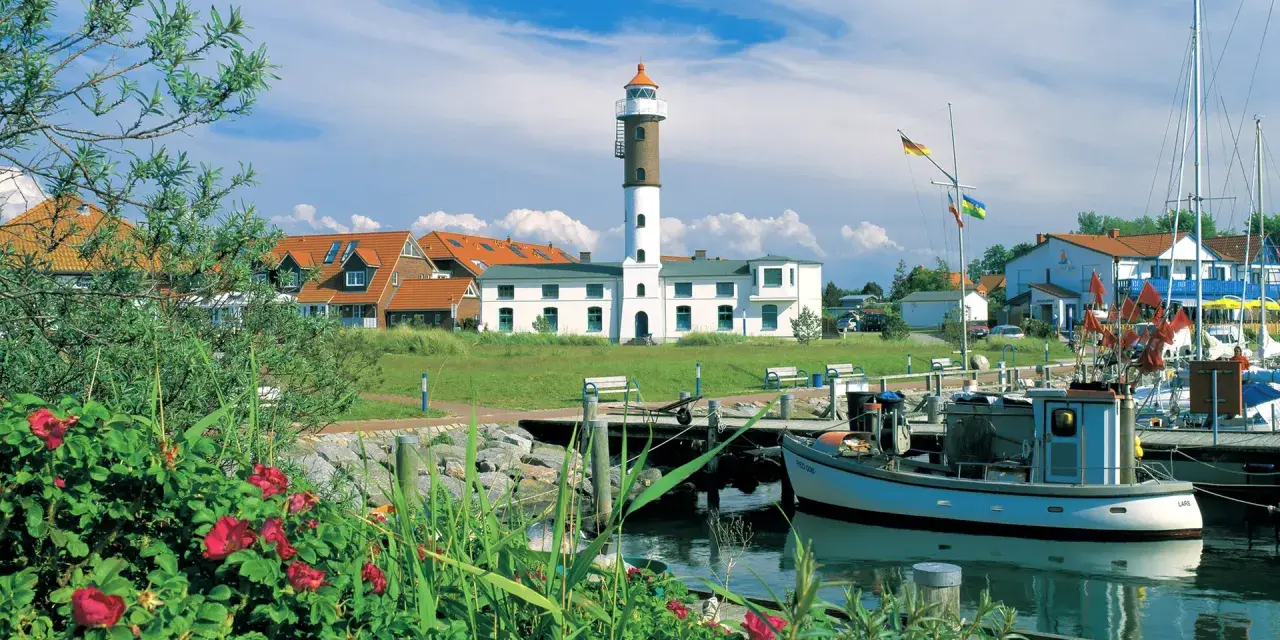 Idyllischer Hafen mit Leuchtturm auf Insel Poel, ein echter Geheimtipp. Boote liegen im Wasser, rote Rosen blühen.