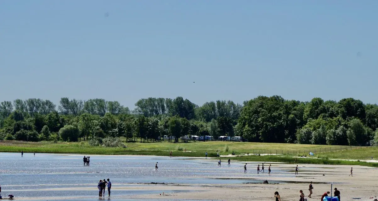 Menschen genießen einen sonnigen Tag am Greifswald Strand. Camper stehen im Hintergrund, während Kinder und Erwachsene im flachen Wasser planschen.