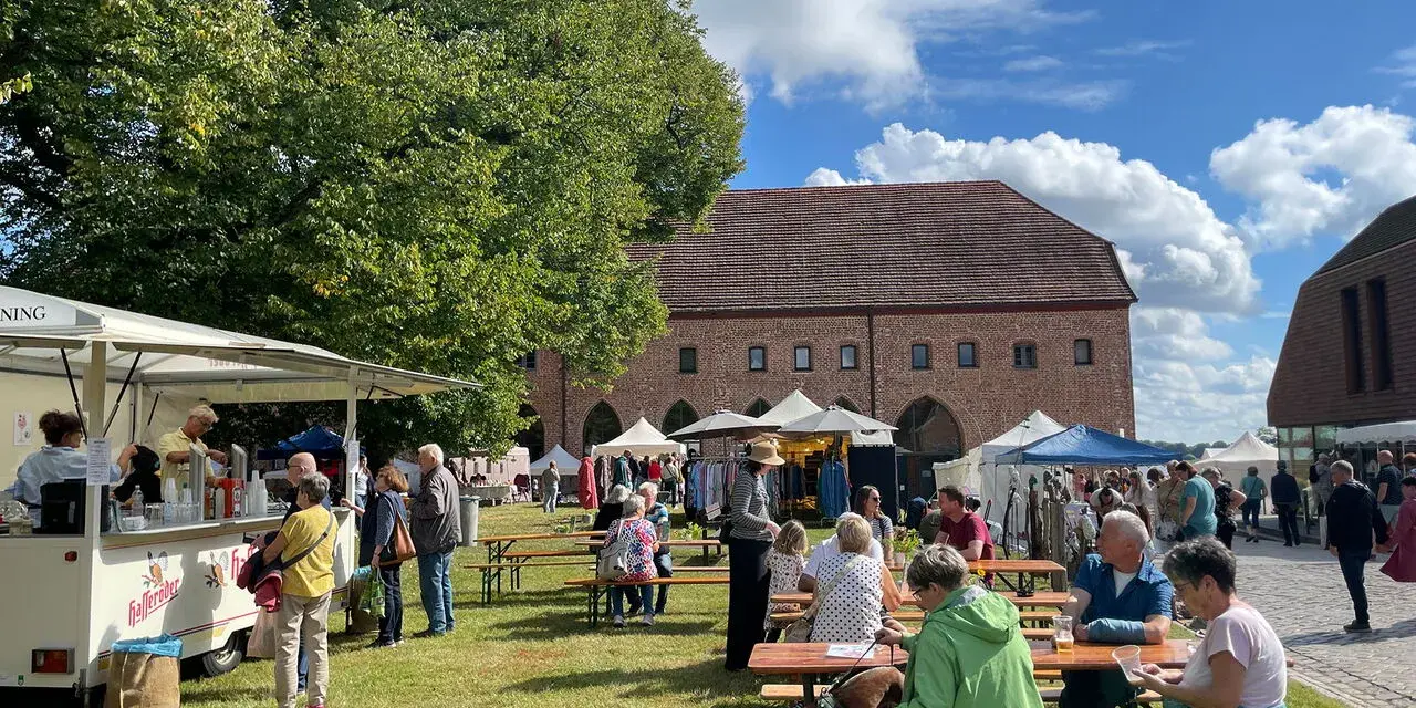Sommerliche Zarrentin Veranstaltungen: Menschen genießen ein Fest mit Ständen und Sitzgelegenheiten im Freien vor historischen Gebäuden.